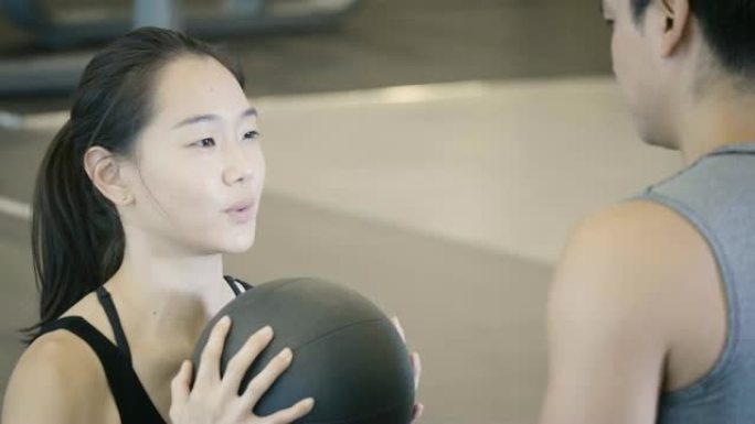 迷人的亚洲女孩在健身馆的私人教练旁边用球做仰卧起坐的特写镜头。