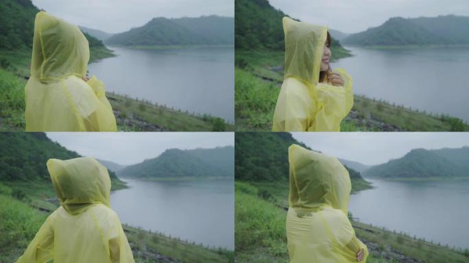 年轻的亚洲女子穿着雨衣站在湖边，在雨中玩耍时感到快乐。生活方式女性在雨天享受和放松。