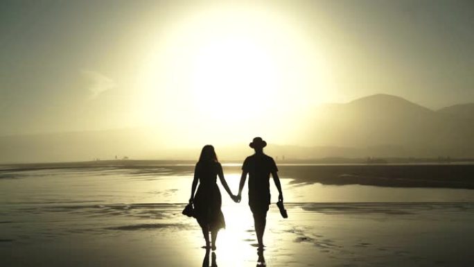 恋爱中的情侣在日落时在海滩上大热天散步