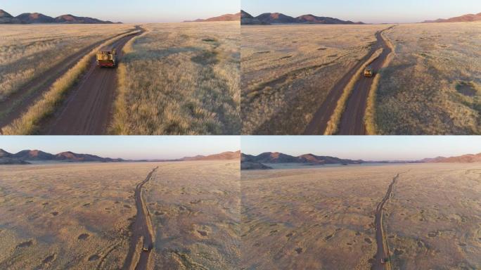 4k高空中后视图，一辆4x4野生动物园车辆在沙路上行驶，穿过非洲萨凡纳草原，与著名的仙女圈，纳米比亚