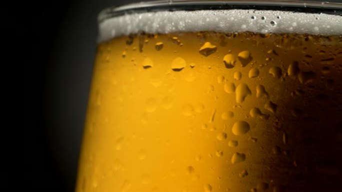 啤酒杯特写。潮湿的旋转玻璃，在黑暗的背景上充满金色的冷却泡沫饮料。引人注目的、吸引人的、开胃的广告式