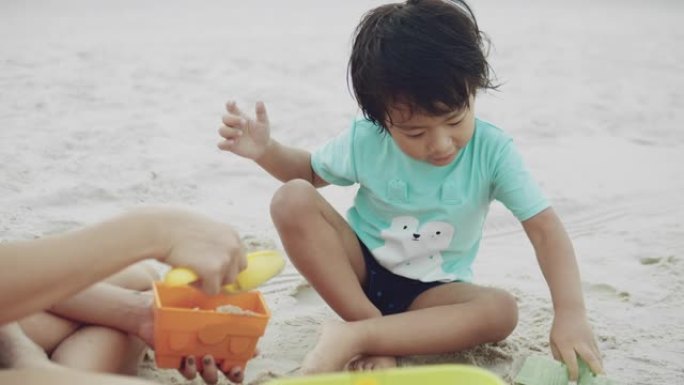 可爱的男婴和年轻的母亲在沙滩上玩沙子。