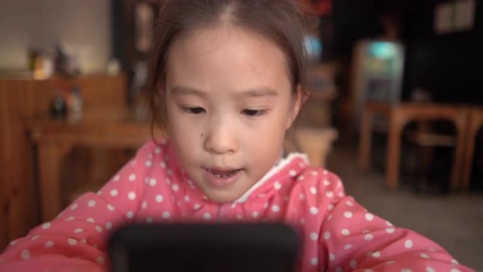 美丽的儿童女孩在日本餐厅玩智能手机游戏