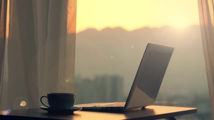日落时分，木桌上的笔记本电脑靠窗户