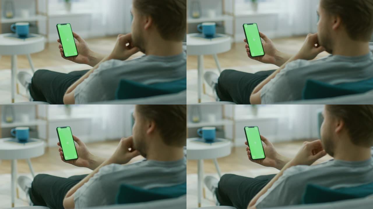 家里的年轻人使用绿色模拟屏幕智能手机。她坐在他舒适客厅的沙发上。肩膀上的相机拍摄
