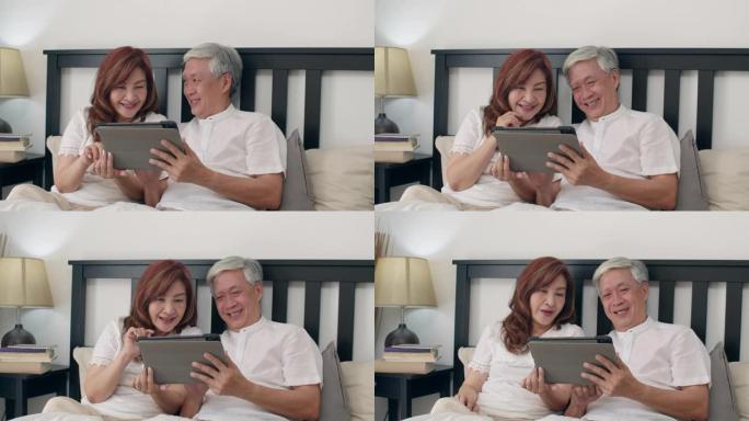 亚洲老年夫妇在家使用平板电脑。亚洲资深的中国祖父母，丈夫和妻子醒来后很开心，早上在家里的卧室里看电影
