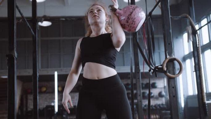 年轻漂亮的运动红头发女人举起壶铃的重量，在大型健身房做功能性训练锻炼。