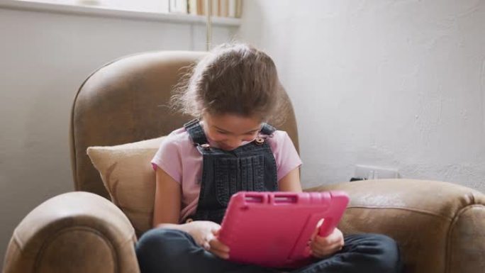 女孩坐在家里的扶手椅上玩数字平板电脑