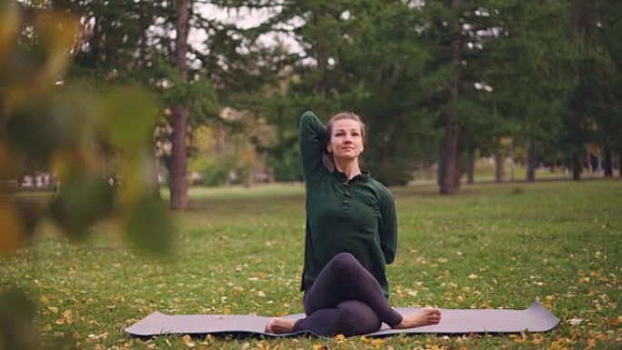 在城市公园的户外练习中，开朗的女士正在公园里锻炼，坐在牛脸姿势，双臂背在背后。自然、千禧一代和健康概