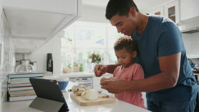 千禧一代的黑人父亲和蹒跚学步的儿子在厨房里一起准备食物，侧视图，特写