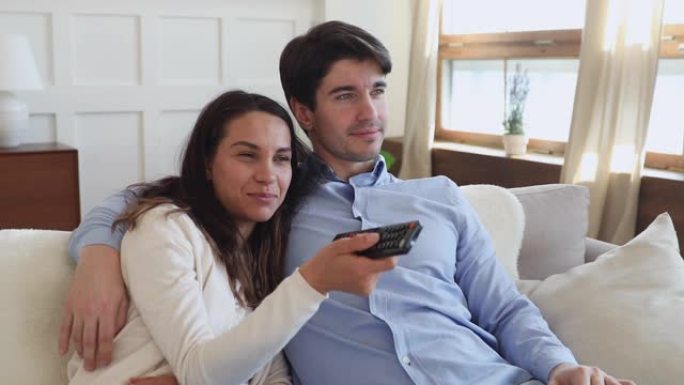 快乐的千禧一代夫妇在沙发上拿着遥控器看电视