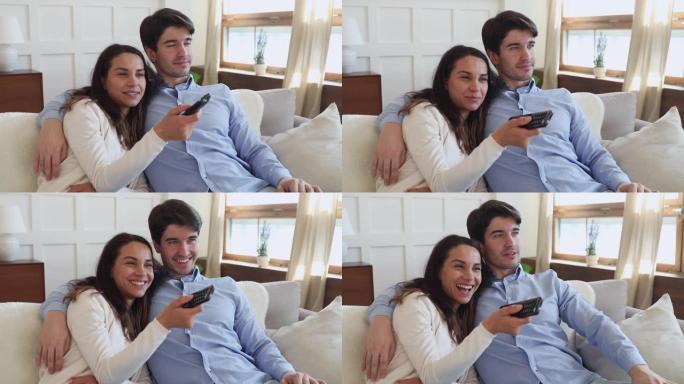 快乐的千禧一代夫妇在沙发上拿着遥控器看电视