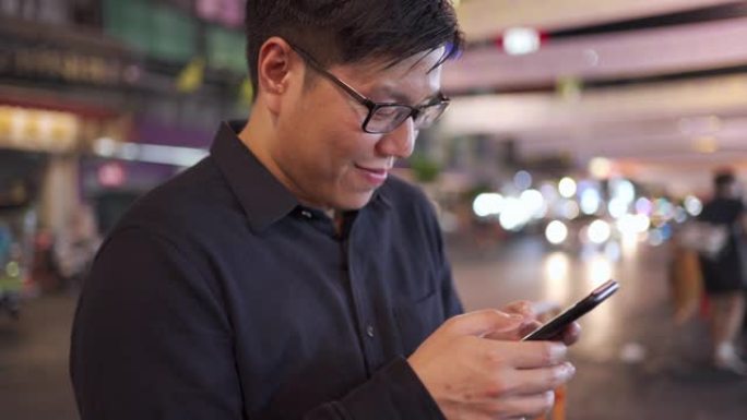 亚洲男子在泰国曼谷姚瓦拉特路等出租车时使用智能手机