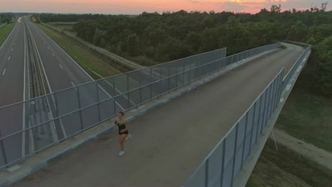 空中女子在日落时跑过桥