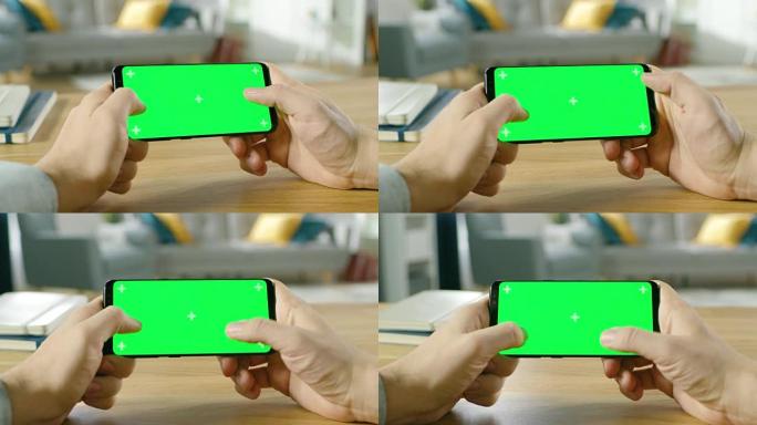 第一人称特写的男子手持绿屏智能手机在横向模式下，用拇指玩游戏。