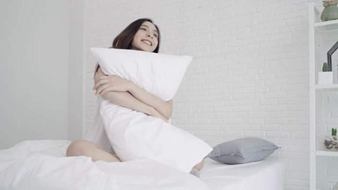 快乐美丽的亚洲女人醒来，微笑着在卧室的床上伸展双臂。年轻的亚洲女性在家使用放松时间。生活方式女人在家