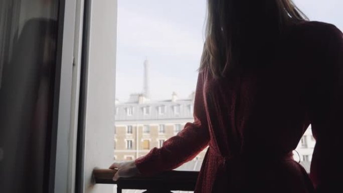 穿着红色连衣裙的美女的特写幻灯片站在法国阳台的窗户上，享受埃菲尔铁塔的慢动作。