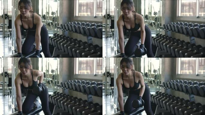 迷人的亚洲女性在健身房锻炼的前视图，用哑铃锻炼肌肉。慢动作。医疗保健、运动和运动概念。