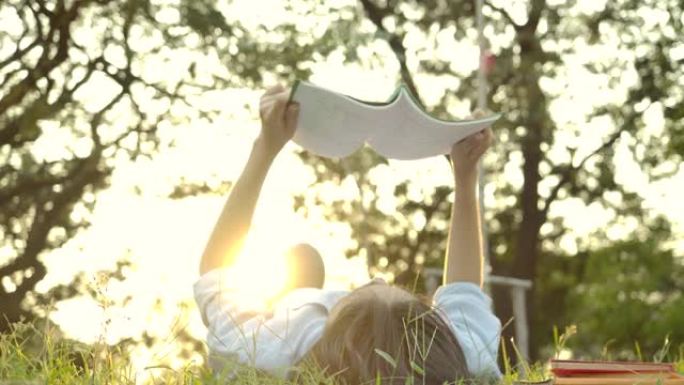 日落时，年轻迷人的亚洲女性在公园的绿草地上躺着看书的慢动作镜头。