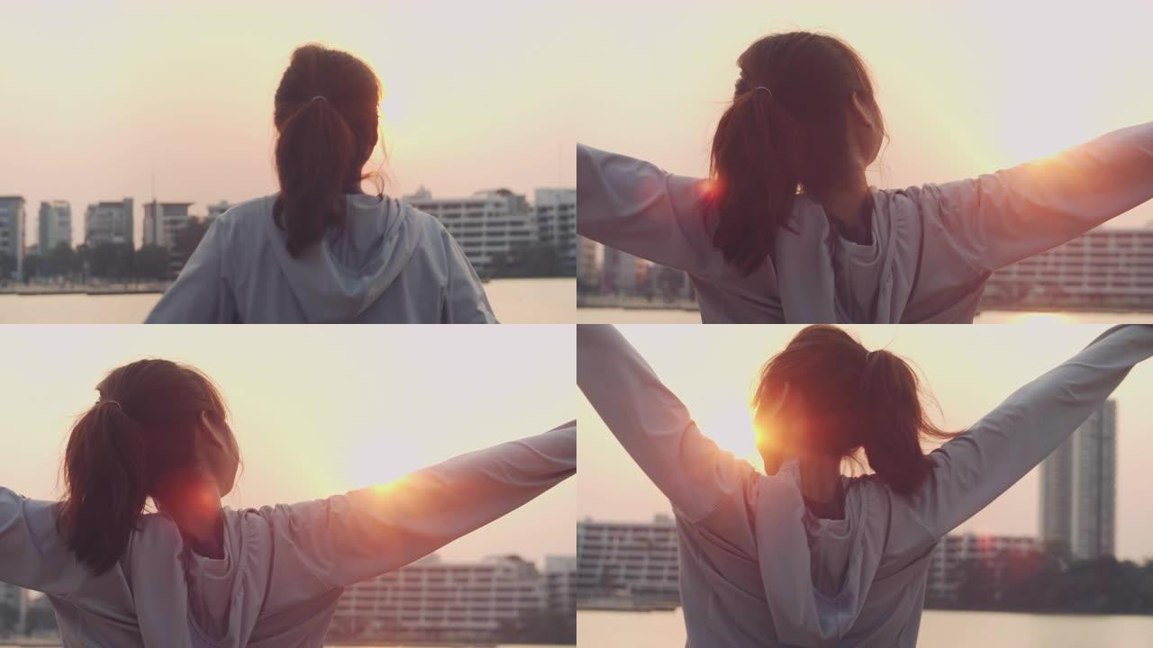 年轻女子张开双臂，看着城市的日落。