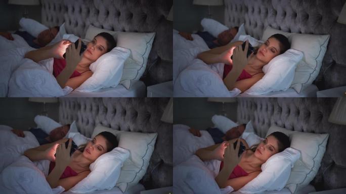 女人躺在床上检查手机，而男人睡在她旁边