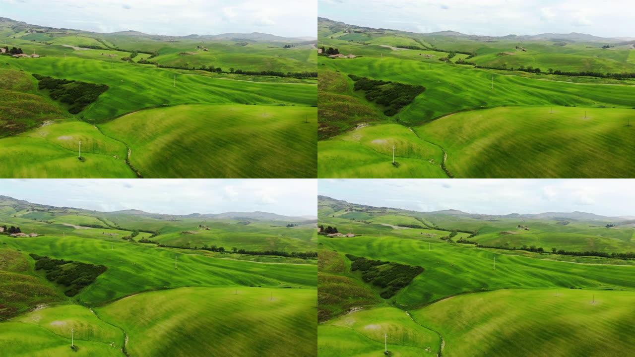 空中电影无人机可以看到有丘陵和田野的乡村。背景与农村绿地，房屋很少。晴天。