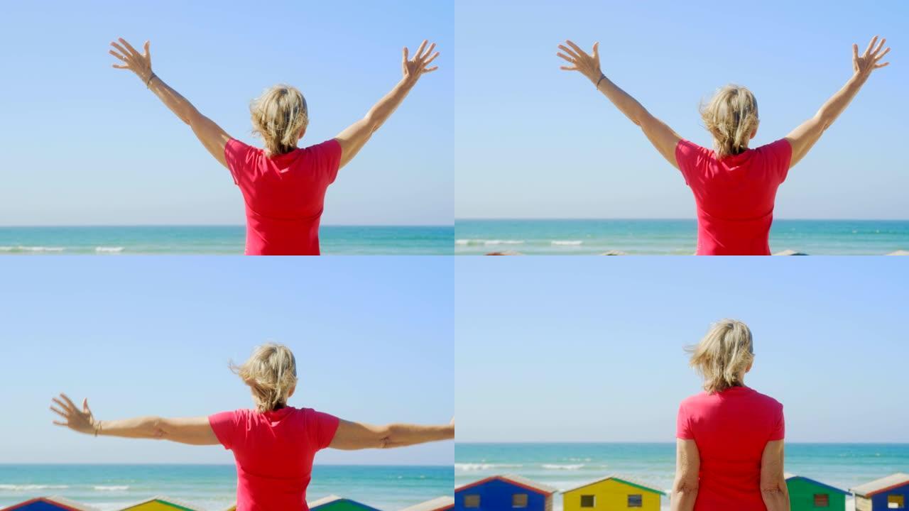 活跃的白人女性站在海滩4k长廊上伸出双臂的后视图