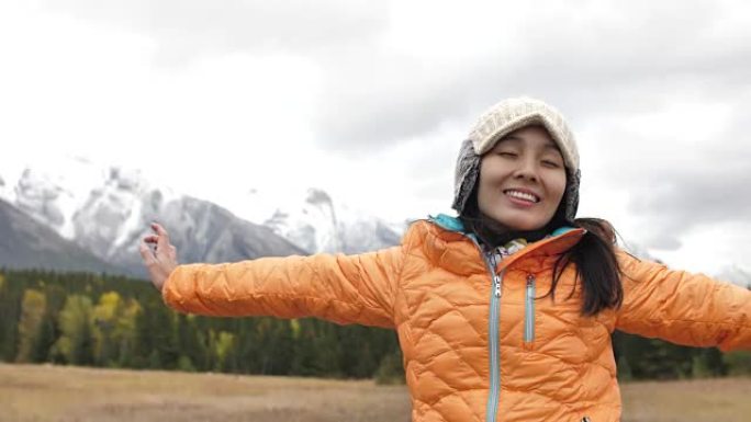 年轻的亚洲妇女在雪山上伸出双臂