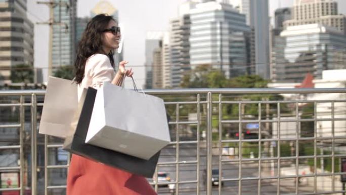 年轻快乐的漂亮女人在城市里带着购物袋散步