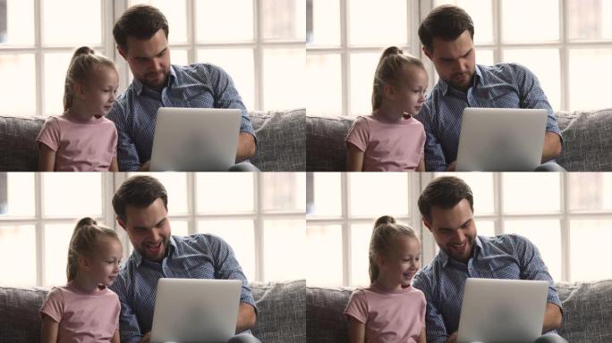 微笑的父亲在笔记本电脑上向小女儿展示有趣的视频。