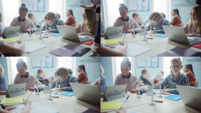 在小学: 一班才华横溢的幼儿作为一个团队使用平板电脑对风力涡轮机进行编程。教室里有孩子学习环保形式的