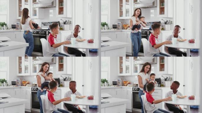 抱着婴儿的母亲站在厨房里与儿子和他的朋友聊天，去玩约会