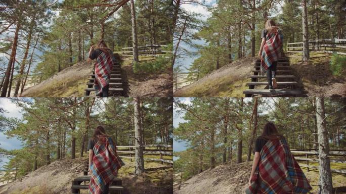 年轻漂亮的女孩走在松林边缘的木制楼梯上，从美丽的蓝色海景出发。温暖阳光明媚的日子与大自然。她裹着格子