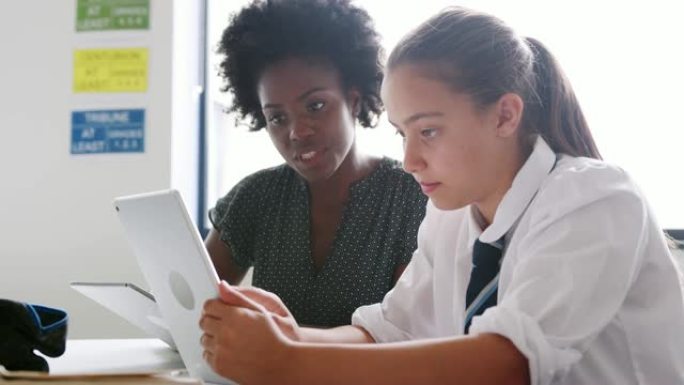 带数字平板电脑的女高中导师给女学生在办公桌上穿制服一对一的学费