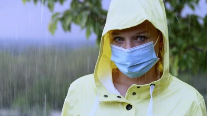 穿着雨衣的SLO MO女人在雨中站着时戴着口罩