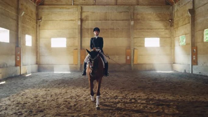 穿着专业服装的年轻女马术大师的电影慢动作，然后在骑马大厅练习赛马和盛装舞步比赛