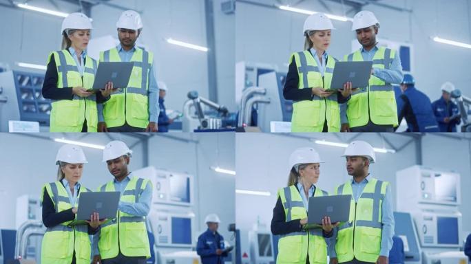 总工程师和项目经理穿着安全背心和安全帽，在现代工厂使用笔记本电脑，交谈，优化生产线。工业设施: 从事