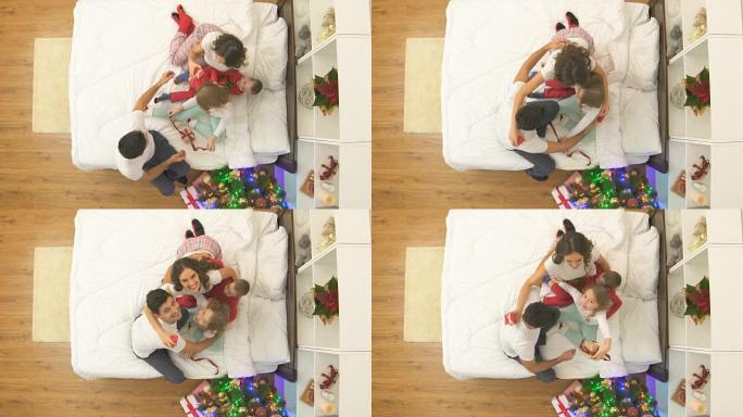 幸福的一家人坐在床上，在圣诞树附近有礼物。从上方观看