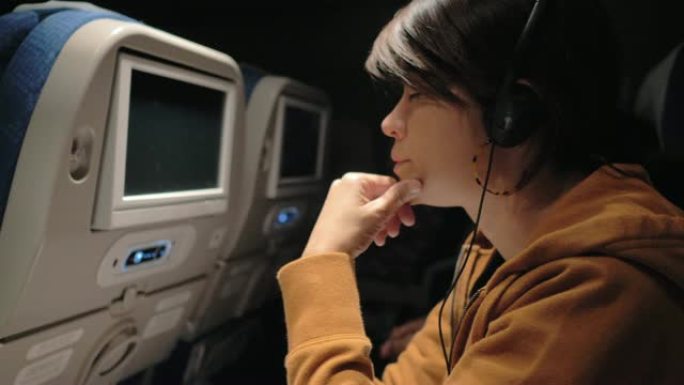 亚洲女性在飞机上在智能手机上选择和听音乐。