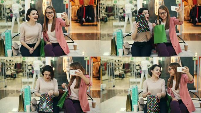 可爱的女孩正在使用坐在购物中心长椅上的智能手机进行在线视频通话，看着手机摄像头，并用纸袋展示购买的物