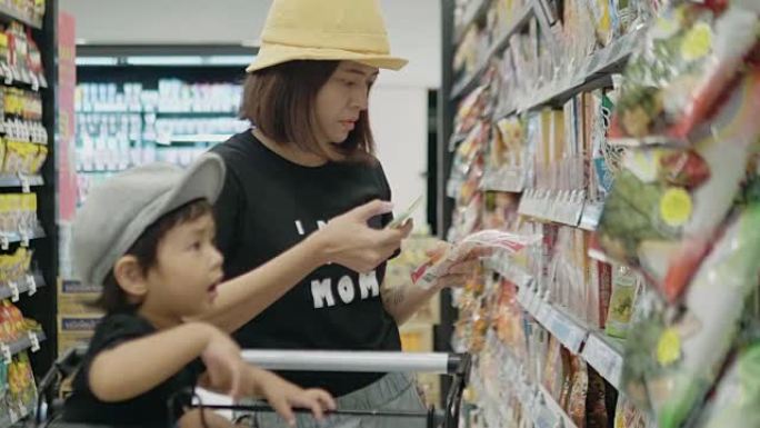 年轻的母亲和她的男孩在超市使用智能手机。