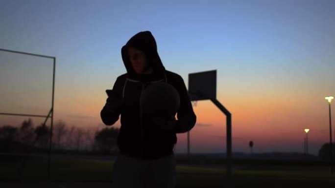 MS Young man使用智能手机并在黄昏时离开室外篮球场