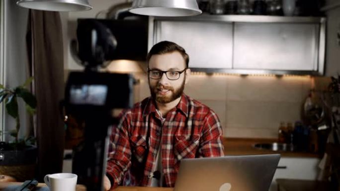 快乐的年轻高加索科技博主男子在家庭厨房慢动作用专业相机为vlog制作视频。