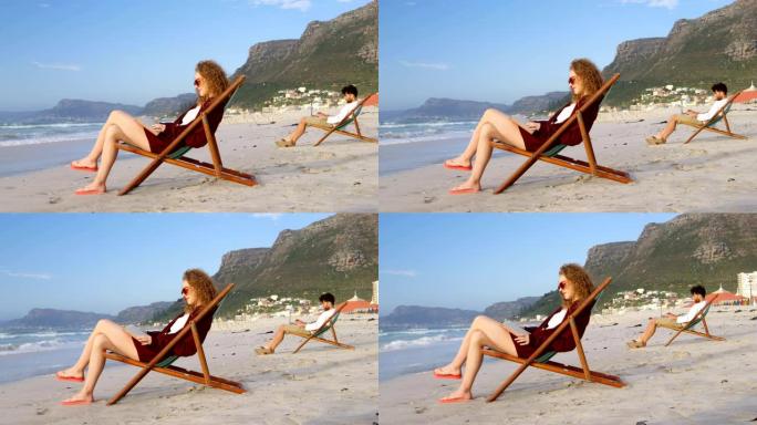 年轻的白人妇女的侧视图，戴着太阳镜坐在躺椅上，在4k海滩看书