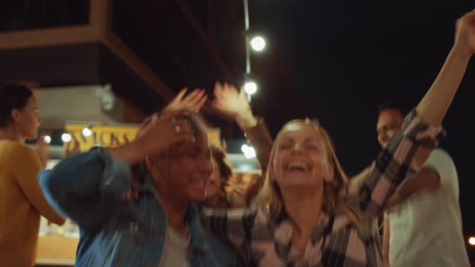 一群朋友正在街头食品汉堡咖啡馆外面举行聚会。两个漂亮的女孩拥抱着音乐跳舞。今天是现代社区的夜晚。每个
