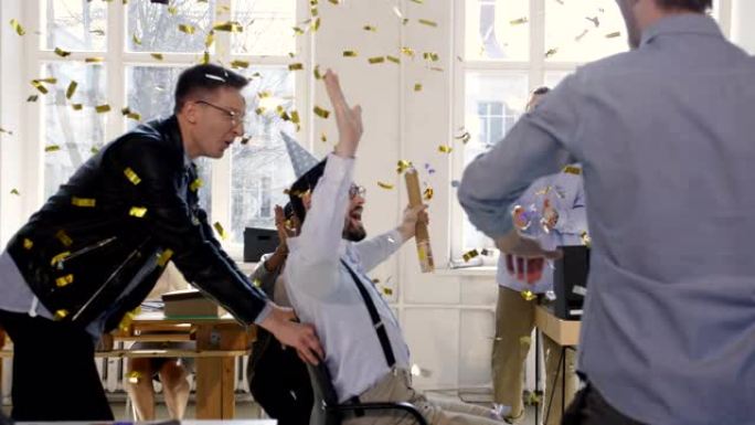兴奋有趣的商人与五彩纸屑一起庆祝胜利，快乐的高加索男性老板骑着办公椅。