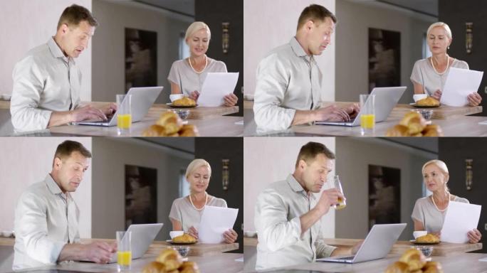 快乐的高加索夫妇吃早餐，用笔记本电脑支付账单