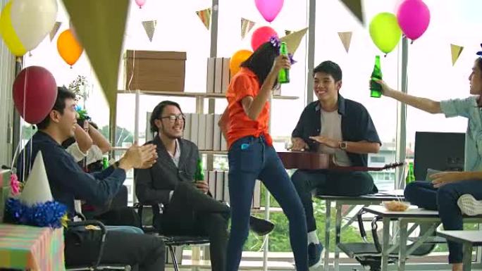 一群年轻人跳舞，玩得开心，在办公室里用烤面包和叮当响的举杯庆祝。慢动作镜头