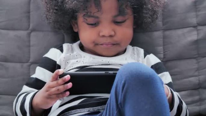 快乐的非洲裔美国孩子使用智能手机观看卡通在家里玩得开心。家庭，肖像，创新，人，教育，生活方式，技术，