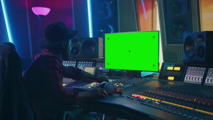 在音乐唱片工作室工作的时尚音频制作人，使用绿屏色度键电脑显示器、混音器板均衡器和控制台来创作新的热门